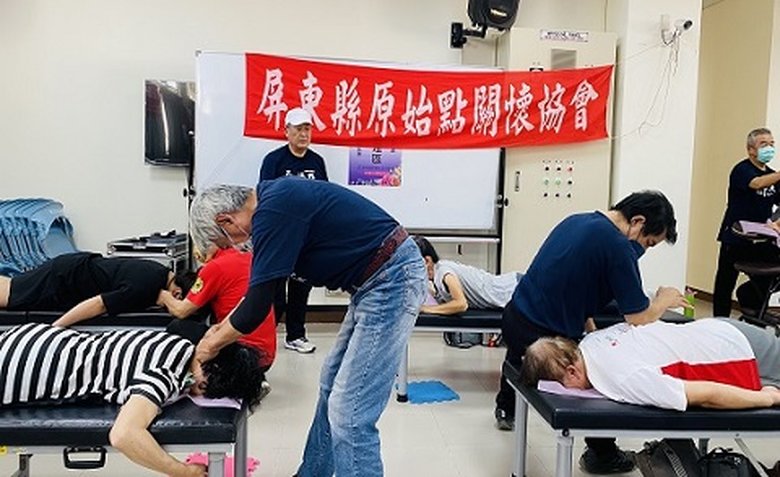 在室內活動場地內，工作人員與參與者在活動現場交流合影，背景掛有公益活動紅布條。